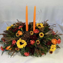 Low floral centerpiece with two orange taper candles and mixed autumn blooms