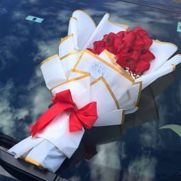 Bouquet of red roses wrapped in white paper with gold trim and a red bow