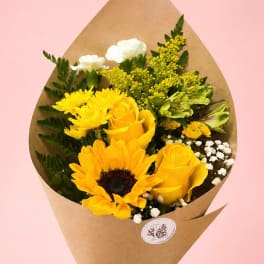 Yellow bouquet with roses, a sunflower, and white filler flowers in brown paper