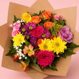Mixed bouquet of roses, daisies, carnations, and alstroemeria in brown paper