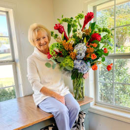 Woman holding a large mixed bouquet in a glass vase by a window