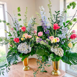 Tall floral arrangements in gold vases with roses, hydrangeas, and delphinium