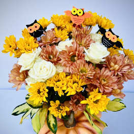 Bouquet of yellow and peach flowers in a pumpkin vase with owl picks