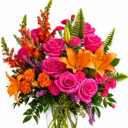 Bright mixed bouquet of pink roses, orange lilies, and orange snapdragons in a glass vase