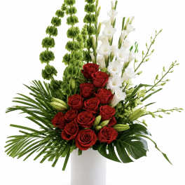 Red roses and white orchids in a white vase with tall green accents