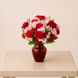 Red roses and pink carnations arranged in a red glass vase
