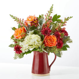 Mixed bouquet of orange, red, and white flowers in a red ceramic pitcher