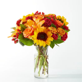 Bright mixed bouquet in a clear glass vase with sunflowers and orange roses