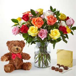 Mixed roses in a glass vase with a teddy bear and chocolates