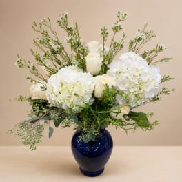 White roses and hydrangeas in a blue vase with airy greenery