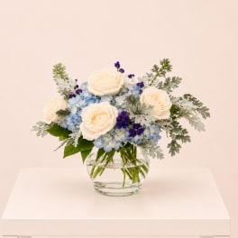 Cream roses and blue flowers in a clear glass vase