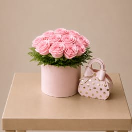Pink roses in a round box with a small polka-dot gift bag beside it