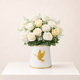 White roses and hydrangeas in a white vase with a gold dove design