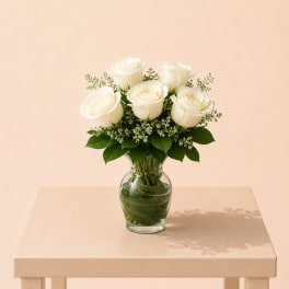 White roses arranged in a clear glass vase with greenery
