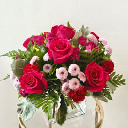 Pink and red rose bouquet with small pale pink blooms in a clear square vase