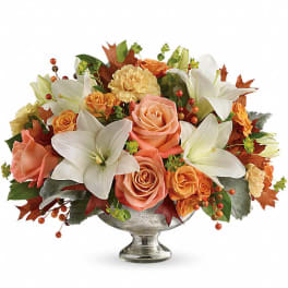 Low centerpiece of white lilies and peach and orange roses in a silver pedestal bowl