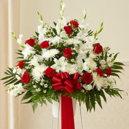 Tall red and white standing floral spray in a white container with a large red bow