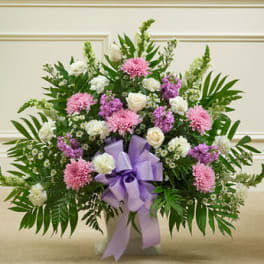 Fan-shaped arrangement of pink, white, and lavender flowers with a large lavender bow in a white container