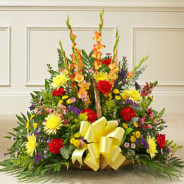 Bright mixed flower basket with yellow, red, and purple blooms and a large yellow bow
