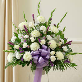 Standing white and purple sympathy arrangement with carnations, mums, roses and a large lavender bow on an easel