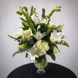 White lilies and pale hydrangeas arranged in a clear glass vase