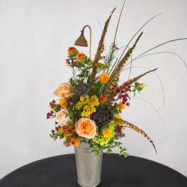 Tall mixed flower arrangement in a clear vase with peach roses and orange blooms