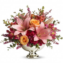Low arrangement of pink lilies, orange and dark pink roses in a silver pedestal bowl