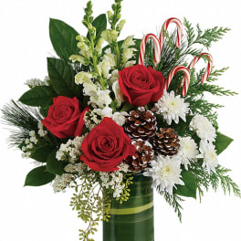 Christmas arrangement with red roses, white flowers, pinecones, and candy canes in a green-wrapped glass vase