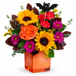 Orange and yellow flowers in an orange glass vase with a bat decoration