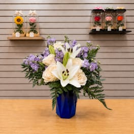 Bouquet of white lilies, cream roses, and purple flowers in a blue vase