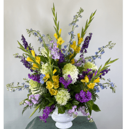 Tall mixed bouquet in a white vase with yellow, purple, blue, and white flowers