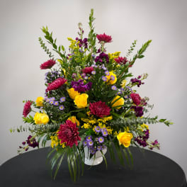 Mixed bouquet of yellow roses, purple blooms, and magenta flowers in a white vase