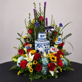 Large floral arrangement with red roses, lilies, and blue hydrangeas around a blue-and-white vase