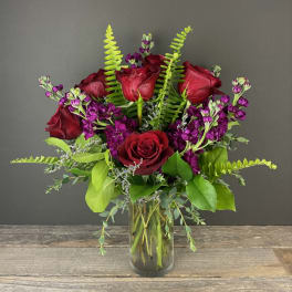 Bouquet of red roses and purple flowers in a clear glass vase
