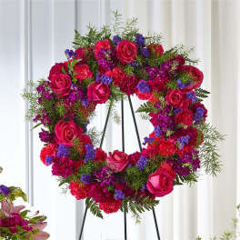 Heart-shaped floral wreath with pink roses and purple flowers on a stand
