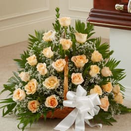 Basket arrangement of peach roses and white filler flowers with a large white bow
