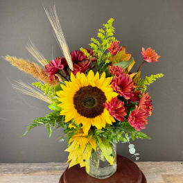 Sunflower and burgundy chrysanthemum arrangement in a glass vase