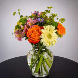 Mixed bouquet of orange, yellow, pink, and purple flowers in a clear glass vase