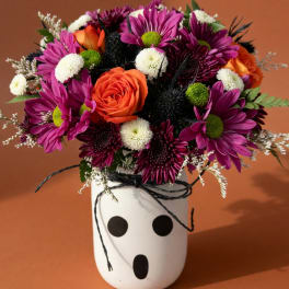 Bouquet of orange roses and purple daisies in a white vase with black dots