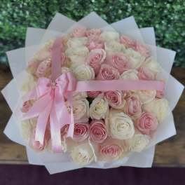 Bouquet of pink and white roses wrapped in white paper with a pink ribbon