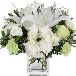 White lilies and roses in a clear glass vase with green accents