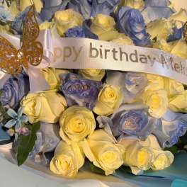 Bouquet of pale yellow and blue roses with a birthday ribbon