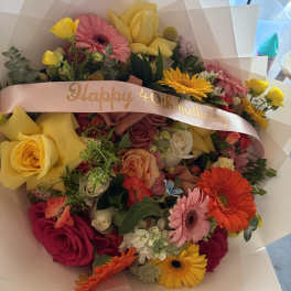 Mixed bouquet with roses, gerbera daisies, and yellow tulips, wrapped with a birthday ribbon
