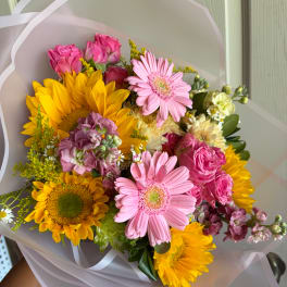 Bouquet of pink gerbera daisies, yellow sunflowers, and pink roses wrapped in white paper