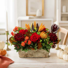 Autumn floral arrangement with red roses and orange lilies in a rustic container