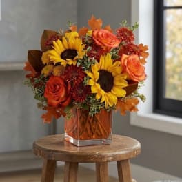 Autumn bouquet with sunflowers and orange roses in a square glass vase