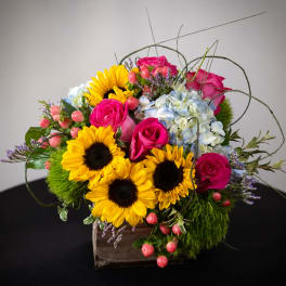 Bright bouquet with sunflowers, pink roses, and blue hydrangeas in a wooden box