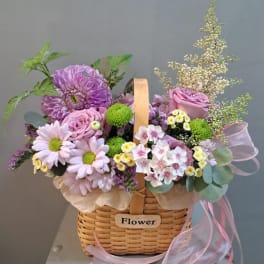 Basket arrangement of pink and purple flowers with a ribbon handle