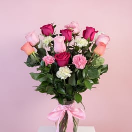 Pink and magenta roses with carnations in a glass vase tied with a pink ribbon