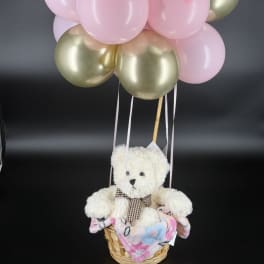 Teddy bear in a basket with pink and gold balloons above